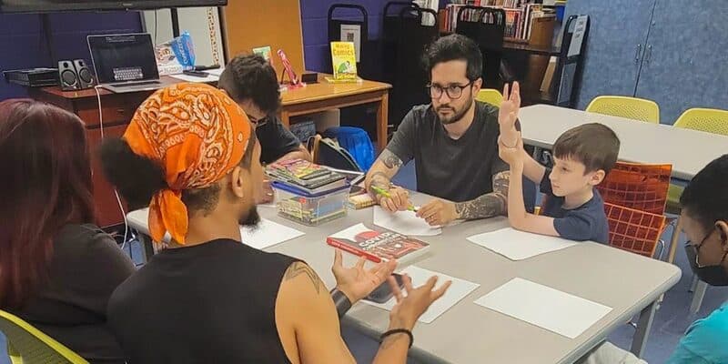 Teens and a librarian talking around a table at a library comics program